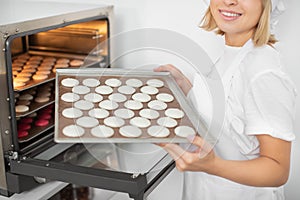 Close up cropped shot of young cheerful girl confectioner in the pastry workshop, holding the baking tray with white