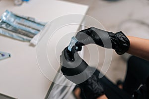 Close-up cropped top view of unrecognizable dentist in protective gloves opening package with new nozzle for polishing