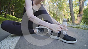 Close-up cropped view of female legs slim athletic woman wears black leggings tracksuit sitting on track in city park