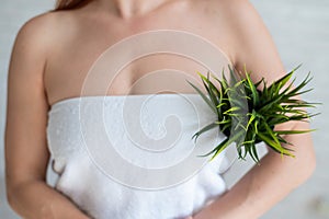 Close-up. Cropped. A woman in a white towel holds an armpit in a pot with a plant simulating unwanted vegetation on her