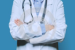 Close-up of crossed arms of female doctor in white lab coat on blue background