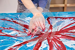 Close-up of crossed hands of woman artist stained with paint painting with rope abstract picture of flower on canvas.