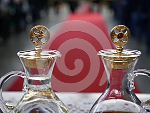 Close up of cruets with water and wine ready for catholic mass with red carpet and people in the background