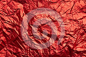 Close-up of crumpled silver aluminum foil texture in red tone. Abstract background, use for design.
