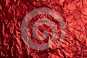 Close-up of crumpled silver aluminum foil texture in red tone. Abstract background, use for design.