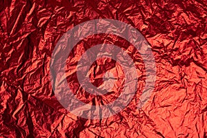 Close-up of crumpled silver aluminum foil texture in red tone. Abstract background, use for design.