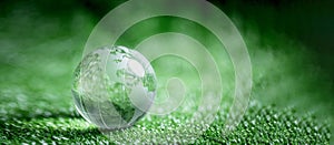 Close up of crystal globe resting on green grass with blur nature background, earth day or world environment day concept. Green