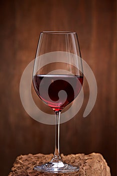 Close-up of crystal half-ful wineglass with red wine standing on wooden stand against wooden background.