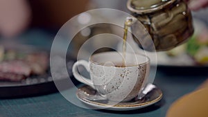 Close-up of cup on cafe table with unrecognizable man pouring healthful tasty tea inside. Young Caucasian guy enjoying