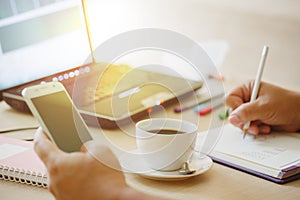 Close up cup of coffee and laptop computer with hand of business man using smart phone.