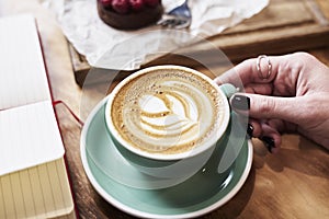 Close-up cup of coffee latte on wooden table in woman hands from above. Having lunch in cafe