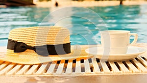 Close-up of a cup of coffee and a straw hat on the background of a blue swimming pool on a summer sunny day. Good