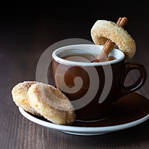 close up of a cup of tea with sugar cinnamon coated donuts against a dark background.