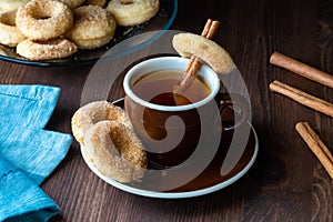 Close up of a cup of tea with sugar cinnamon mini donuts against a dark background.