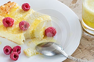 Close-up of curd casserole with raspberries, honey and spoon on white plate and glass with smoothie on wooden cut.