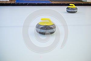 Close-up of a curling stone with a yellow handle stands on ice