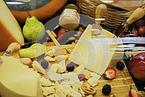 Close-up of cut Cheese with knife on wooden board and fruit on showcase on counter at store, real scene in food market