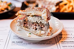 Close up cut half of Cheeseburger with grilled beef, feta cheese and sliced tomato served in white plate