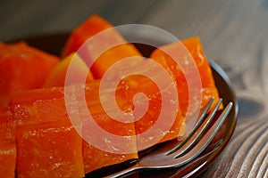 Close-up of cut, ripe red-fleshed Papaya fruit on a brown saucer, on table top