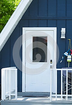 Close up of cute adorable A frame triangle shaped house or home with deep blue color with white door, wood front porch railing,