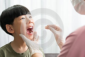 Close up of cute Asian boy smile and open mouth getting saliva swab antigen test by mother wearing latex glove at home