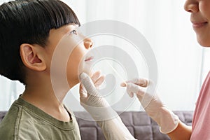 Close up of cute Asian boy wear white medical face mask getting nasal swab antigen test by mother wearing latex glove at home