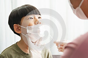 Close up of cute Asian boy wear white medical face mask getting nasal swab antigen test by mother wearing latex glove at home