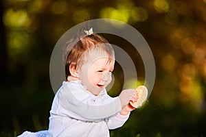 Close-up of cute baby girl sitting in the park and eats the snack at warm day.