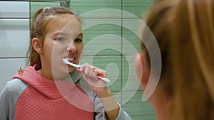 Close-up cute beautiful female child with fair hair brushes her teeth thoroughly in mirror reflection