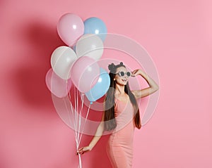 Close-up of cute blond girl standing in a studio, smiling widely and playing with blue and pink baloons.