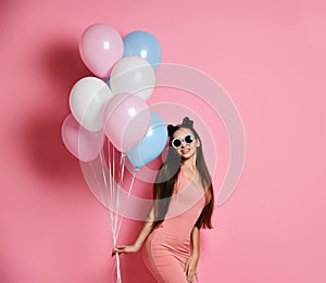 Close-up of cute blond girl standing in a studio, smiling widely and playing with blue and pink baloons.