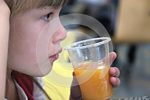 Close up of cute child girl drinking orange juice from plastic cap in a restaurant