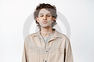 Close up of cute curly guy kissing, pucker lips and looking funny at camera, white background