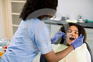 Close-up of cute curly mixed raced girl with open mouth during oral checkup at the dentist. Young female African