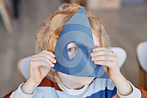 Close-up of cute gingerhaired little boy looking through hole in blue paper