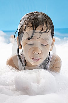 Close up of a cute girl blowing white soap bubbles in her hand in a swimming pool at home.