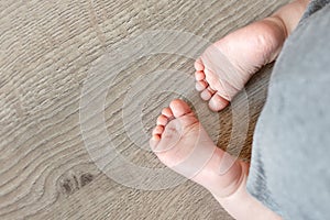 Close-up cute infant baby feet on wooden floor background. Funny adorable heels. Tender childs toe