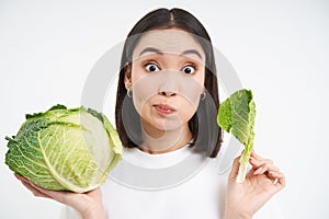 Close up of cute korean woman, eating cabbage, on diet, holding lettuce, isolated on white background