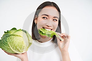 Close up of cute korean woman, eating cabbage, on diet, holding lettuce, isolated on white background