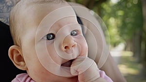 CLOSE UP: Cute little baby girl puts her tiny hand in her mouth while resting in strong dad`s lap.