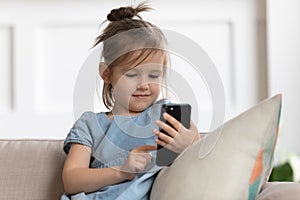 Close up cute little girl holding phone, looking at screen