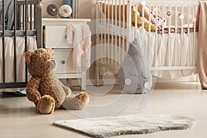 Close-up of a cute teddy bear and a gray raindrop pillow on the floor of a scandi bedroom interior for twins. Real photo