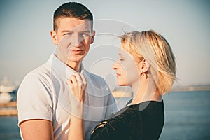 Close up of a cute young beautiful couple at pier at sunset, man hugging his girlfriend softly, hipster, happy smiling