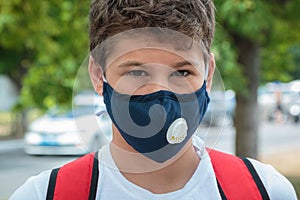 Close up cute young boy with protective mask on his face. Teenager in white t shirt wearing medical mask to protect from corona
