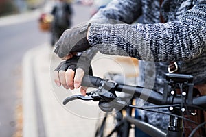 A close-up of a cyclist with electrobike putting on gloves outdoors in town.