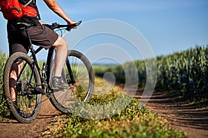 Close-up of cyclist man legs with mountain bike on the path of the green field in the countryside.