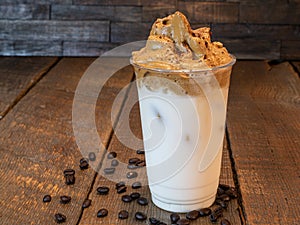 Close-up of Dalgona Whipped coffee in a plastic cup with milk on a wooden background.