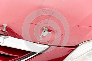 Close up of damaged car hood in the crash accident with hole on the red vehicle and peeled paint