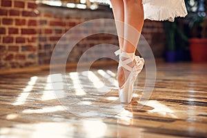 Close-up dancing legs of ballerina wearing white pointe ballet shoes in the dancing hall.