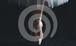 Close-up of dancing legs of ballerina wearing white pointe on a black background